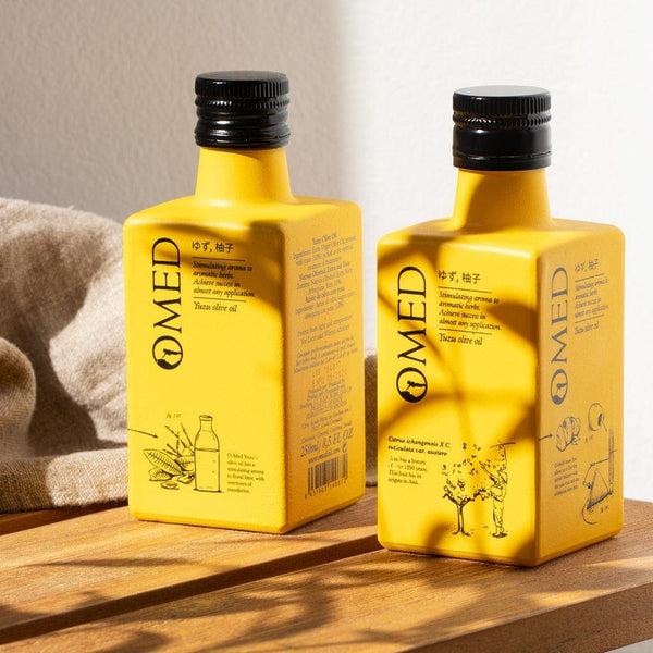 Gros plan de deux bouteilles d'huile d'olive au Yuzu OMED entre ombre et soleil sur un banc
